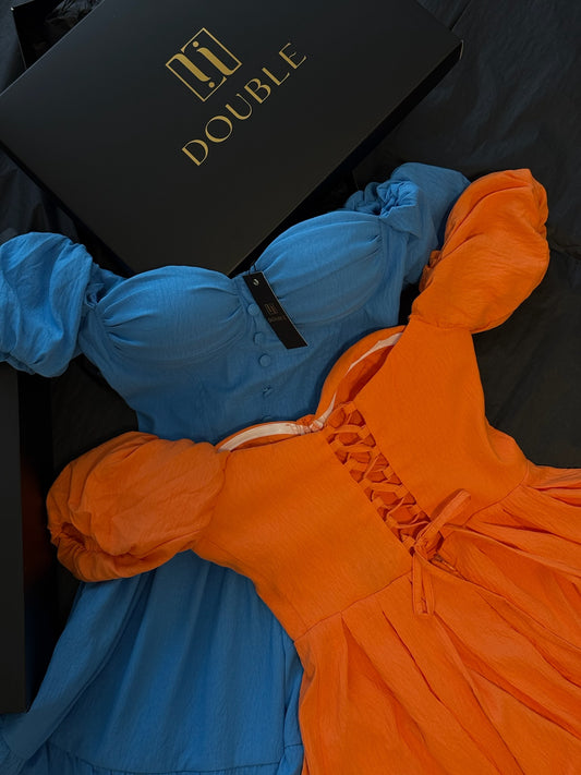 Summer Muse Dress: blue and orange puff-sleeve corset dresses laid flat beside a black DOUBLE box