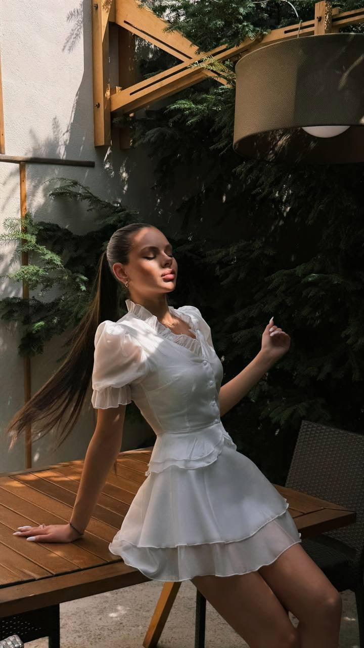 Blouse & Skirt Set: sheer white organza puff-sleeve blouse with tiered mini skirt, worn by a model at a wooden table